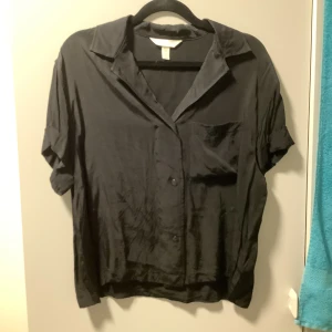 Skjorta från hm  - Kortärmad svart skjorta från H&M i strl XS i satinmatrial, sparsamt använd 