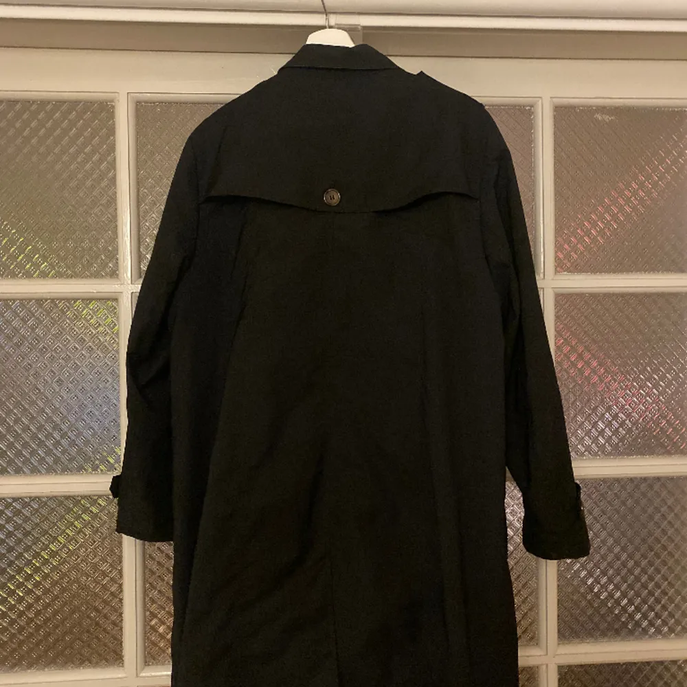 En fin svart kappa/trenchcoat med bruna knappar och coola detaljer. Storleken skulle jag uppskatta till en L. Köpt secondhand, men har inga tecken på användning.. Jackor.