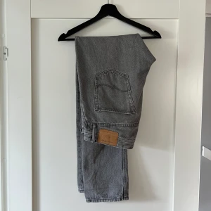 Grå jeans - Ett par grå jeans från Jack & Jones. Relativt använda men i bra skick förutom ett litet slitage längst med vid ett av benen, därav lågt pris