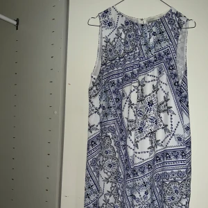 Klänning blå/vit - Mönstrad klänning med gulddetalj. Knälång. 