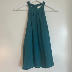 Topp med halterneck - Fin grönblå halterneck-blus som använts ett fåtal gånger. Tyget som sitter runt halsen tas på och av med hjälp av en knapp (se bild 3)💚💚Blusen har ett lite randigt mönster av sömmar som inte syns jättebra i första bilden💚