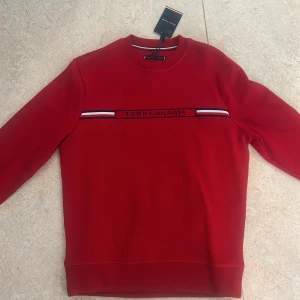 Tröja från Tommy Hilfigher mycket gott skick med prislapp på - Storlek M rödfärgad tröja med Tommy hilfigher tryck på framsidan. Snygg passform. Etiketten sitter fortfarande på och tröjan har ej använts. 