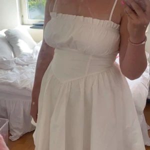 Vit klänning - Supersöt vit klänning med korsettliknande detalj i midjan, piffig underdel och sitter som en smäck! Endast använd en gång på midsommar förra året! 