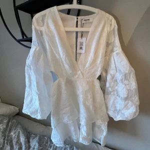 En jättefin oanvänd vit klänning från Showpo. Passar perfekt nu till sommaren eller också för studenten. Orginalpriset var: 800kr - Product Details: Invisible zipper on the centre lower back, Long balloon sleeves with elastic cuffs, Deep V-neckline, Cut outs on the sides  Size & Fit: Size S: 83cm   Model's height: 168cm 