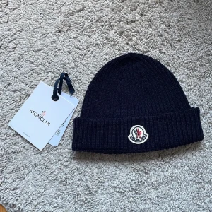 Moncler mössa - Här säljer jag min oanvända riktiga moncler mössa som är använd ändast ett par få gånger. Jag har tyvärr inget kvitto. Men den har nfc scan. Den är navy blue. Pris kan diskuteras.