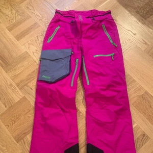 Skidbyxor Bergans of Norway stl M - Ett par skidbyxor i nyskick, cerisrosa med grå ficka, svarta detaljer. Super snygga men för stora för mig. Stl M Saknar hängslen
