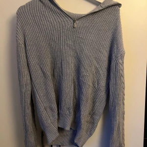 Ljusgrå stickad tröja från Wow - En ljusgrå stickad tröja från Wow med en dragkedja vid halsen. Tröjan har långa ärmar och ribbstickade muddar vid ärmslut och nederkant. Den är varm och bekväm, perfekt för kyligare väder.