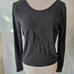 Svart långärmad topp från ONLY - En svart långärmad topp från ONLY med en öppen rygg och knutdetalj. Toppen har en rund halsringning och är tillverkad i ett mjukt material.