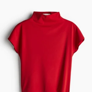 HELT NY! Röd figurnära top - HELT NY! Säljer en stilren röd halvpolotop. Den är ärmlös (holkärm)och har en hög krage som ger en elegant touch. Perfekt för både vardag och fest. Materialet känns mjukt och bekvämt mot huden. Passar XL-XXL