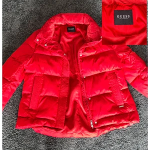 Guess jacka - Säljer en snygg röd pufferjacka från Guess, Jackan är perfekt för vintern med sin tjocka vaddering och avtagbara fuskpäls på huvan samt två fickor med dragkedja. Den har aldrig använts! Kontakta mig för ytterligare information😊