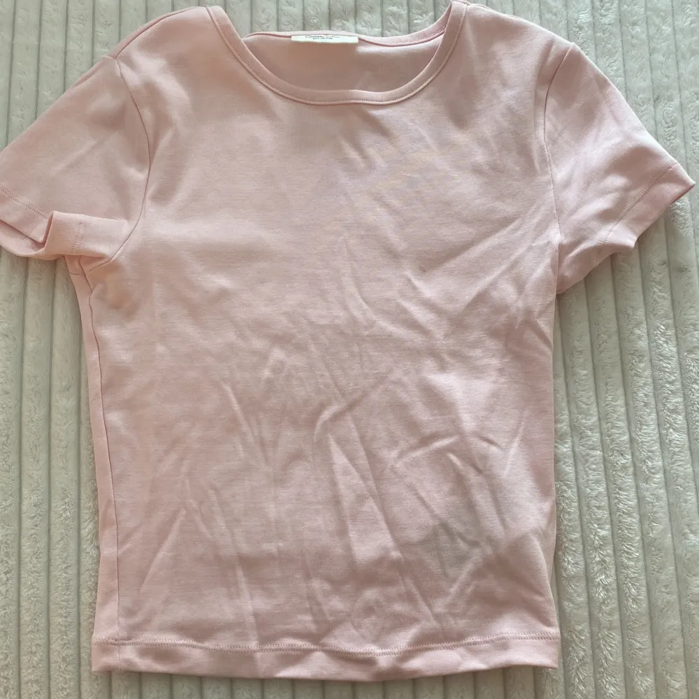 En ljusrosa t-shirt från Gina Tricot, del av kollektionen 'basically basics'. T-shirten har korta ärmar och en rund halsringning. Den är tillverkad i ett mjukt material och har en liten fläck på framsidan som troligtvis går bort i tvätten 💕🌟. T-shirts.