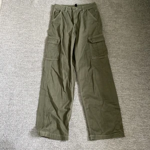 Olivgröna cargobyxor från H&M Divided - Säljer ett par gröna cargobyxor från H&M Divided i storlek 34. Byxorna har flera praktiska fickor och är tillverkade i 100% bomull. De är i  mycket bra skick och knappt använda men med en liten fläck på framsidan. Perfekta för en avslappnad och cool stil! 🌿