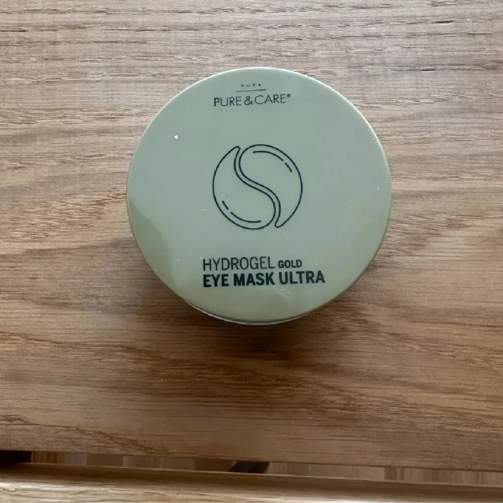 En burk med Hydrogel Gold Eye Mask Ultra från Pure & Care. Förpackningen är grön med vit text och innehåller ögonmasker i hydrogel för att återfukta och vårda huden runt ögonen.. Skönhet.