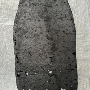 Svart midkjol  - Säljer en superfin svart kjol med blommigt mönster. Kjolen är i storlek S - 36 och har en dragkedja på baksidan. Den är perfekt för festliga tillfällen och har en tight passform som framhäver figuren. Kjolen är knälång - midkjol. Från Lindex