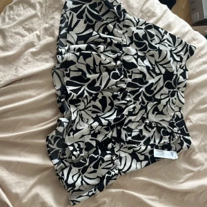 Svartvit blommig kjol - Säljer en snygg svartvit kjolmed blommigt mönster.  Perfekt för sommaren eller en festlig kväll! Aldrig använd med prislappen på! 