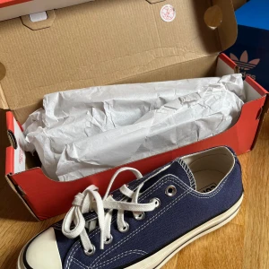 Blå Converse Chuck Taylor All Star - Säljer ett par mörkblå Converse Chuck 70 Ox sneakers i strl 37,5 men passar mig som har strl 38. De är i nyskick och kommer i originalförpackning. Skorna har en gulvit sula vilket ger en mer ”vintage look”. Jag tror skorna är slutsålda i Sverige, så de beställdes från storbritannien, vilket förklarar priset. Perfekta för vardagsbruk och passar till nästan alla outfits! 😊