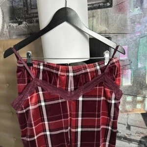 Rutig klänning från Hunkemöller - En rutig set (linne + shorts)  från Hunkemöller med spetsdetaljer. linnen har smala axelband och en v-ringad halslinje. Färgerna är en blandning av röd, vinröd och vit.