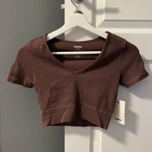 Brun ribbad croppad topp från Bik Bok - Säljer en snygg brun ribbad croppad topp från Bik Bok. Toppen har en v-ringad hals och korta ärmar. Perfekt för en casual look eller att klä upp för en fest. Helt ny med prislapp kvar!🤎