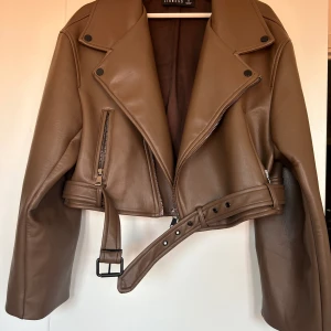 Brun faux läderjacka  - Otroligt snygg jacka i läderimmitation i en mörkare brun färg. Jackan är från Australienska märket Liones i storlek M men passar både S och L skulle jag säga för den kan dras åt med spänne men den är ändå oversized:) använd 1 gång (på sista bilden)😊