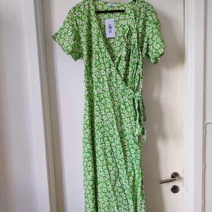 Lång omlottklänning med blomster - Sval ljusgrön omlottklänning med knytband i sidan, aldrig använd.    Färgen stämmer bäst överens med bilderna från hemsidan.  Material: 100% Viskos Nypris 600 kr