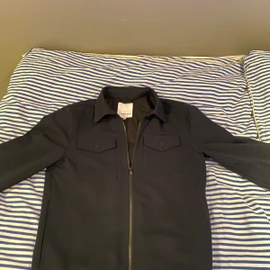 Lindbergh overshirt/jacka - Marinblå overshirt i storleken (M). Hyfsat bra skick förutom ett hål på insidan av jackan men det varken synns eller märks att hålet är där.