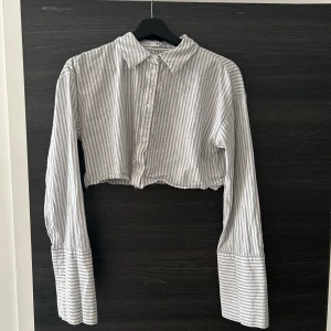 Skjorta  - En randig skjorta med långa ärmar och en kort modell. Skjortan har en knappstängning framtill och en klassisk krage. Hanna Schönbergs kollektion med NAKD