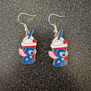 Örhängen med tecknad figur och milkshake - STITCH som håller en milkshake. Örhängena har detaljer i blått, rött, vitt och rosa. krokarna är inköpta som nickelsäkra.