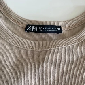 Beige ribbad linnetopp från Zara - En beige ribbad linnetopp från Zara. Toppen är ärmlös och har en rund halsringning. En ribbad grön topp från Weekday. Säljes tillsammans. 