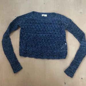 Stickad tröja - En blå stickad tröja från Hollister med ett genombrutet mönster. Tröjan har långa ärmar och en normal passform. perfekt över ett linne, inga defekter, sparsamt använd och perfekt inför hösten