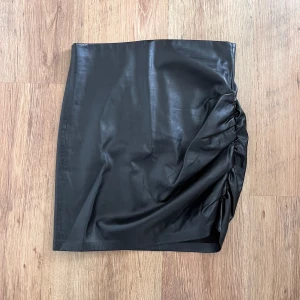 Svart festlig kjol i fake skinn från Zara - Kjol i skinnimitation och passar perfekt till fest eller festival. Kjolen är i fint skick.
