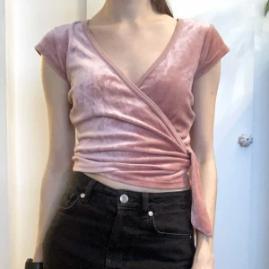 Rosa omlott topp, sammet, stl XS/S, croppad, crop top, ljusrosa, y2k, 90-tal - Ljusrosa kort omlott-topp i sammet. Holkärm samt knytband. Finns en liten gul fläck höger fram på kantbandet till ringningen. Mått i cm: bröstvidd 43; axelbredd 36; längd fram från axeln 46; ärmlängd 7.