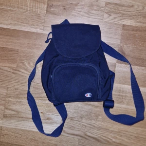 Champion mini-ryggsäck - En vintage champion ryggsäck som är liten men får plats med allt man behöver!! Perfekt på semester och är allmänt snygg. Den är inte i nyskick men inte heller allt för sliten, se skick på bilderna❤️