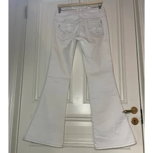 Vita byxor med stjärnor  - Jättesöta lågmidjade/mid-waist utsvängda byxor med stjärnor på fram och bak fickorna och silversömmar. Midjemått, raktöver: 38cm. Innerbensmått: 79cm. Modellen på bilden är 157 cm och byxorna är lite för långa