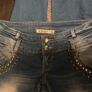 Bootcut lågmidjade jeans - Ljusblå med med mörkgrå bootcut långa i benen och är lågmidjade. Gulddetaljer på fickor bak och fram. Pris går att diskuteras, går att mötas upp i Jönköping 