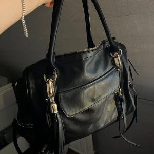 Urban Expressions Väska - Säljer denna svarta väskan från Urban Expressions som köptes på loppis för några år sedan och aldrig kommit till användning. Den har några små skador på utsidan av väskan (skriv för fler bilder) men är annars i väldigt bra skick. 