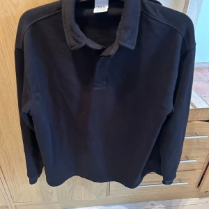Svart långärmad pikétröja från Zara - En svart långärmad pikétröja från Zara. Tröjan har en klassisk krage i marinblå färg