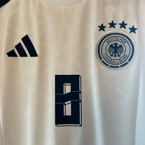 Tyskland EM 2024 #8 KROOS - Tysklands hemmaställ från EM 2024 med Kroos #8 på ryggen, tröjan som han bar under sin sista match någonsin när de tyvärr åkte ut mot Spanien.  Tröjan är en reprint