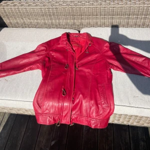 Röd Läderjacka DANIER - Röd läderjacka från DANIER i väldigt fint skick. Köpt för 799 kr på Second hand förra hösten och därefter använd 1 gång. Enda märkbara är en liten defekt på höger arm (se bild) samt lite vit färg vid höger armhåla, vet ej om det går bort i tvätt. 