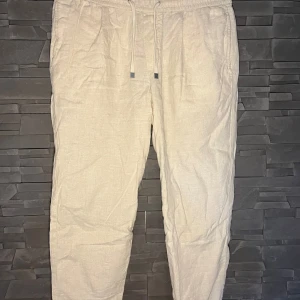 Beige linnebyxor - Ett par bekväma beige linnebyxor med snören i midjan. Byxorna har en avslappnad passform och två bakfickor. Linnebyxorna är sparsamt använda och i mycket bra skick! Nypris 599kr