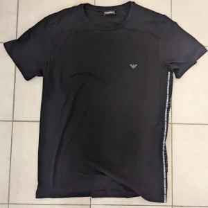 Armani T-Shirt  - Armani T-Shirt svart med text längs vänstra sidan nedåt.