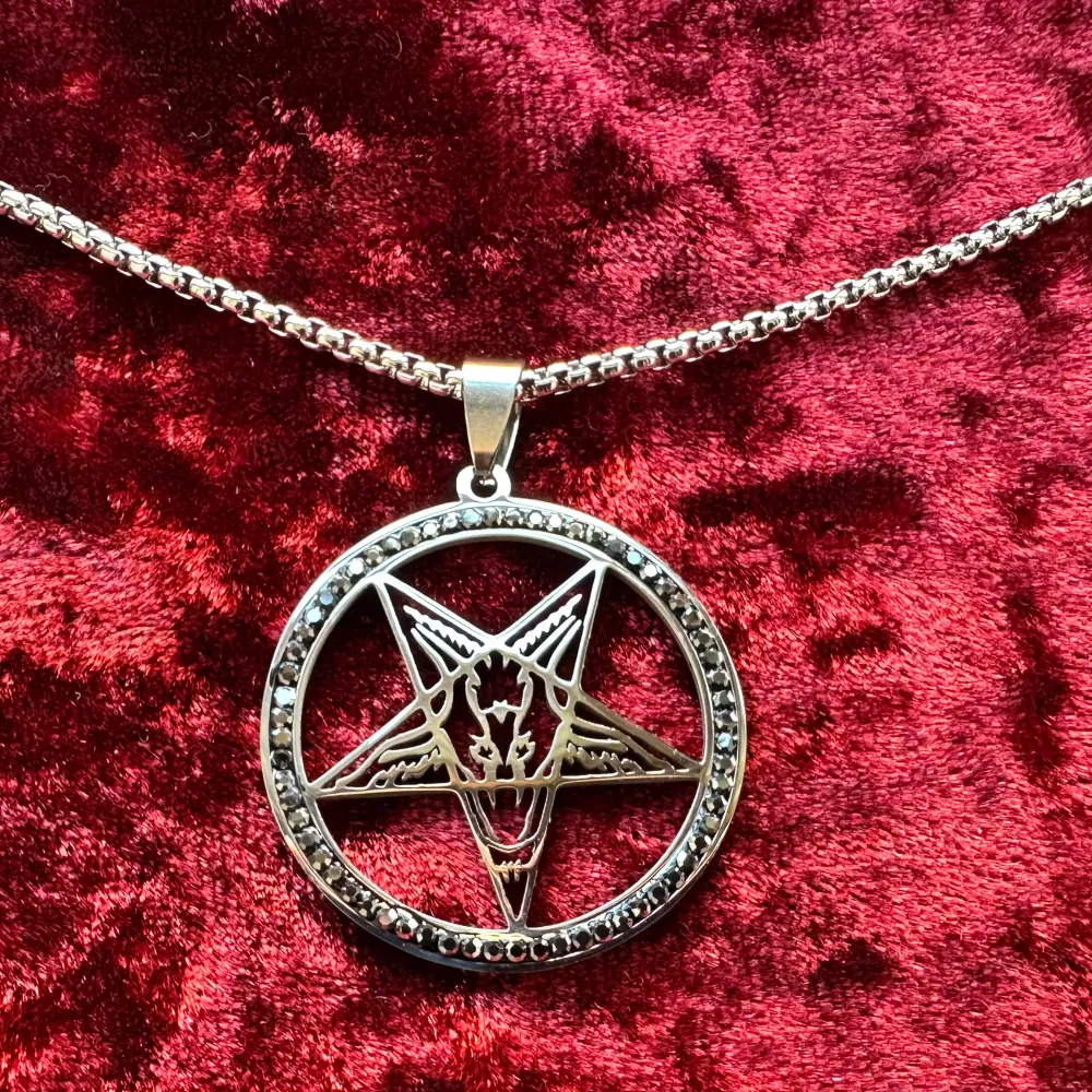 Nytt silverfärgat halsband i rostfritt stål och kristaller med amulett med pentagram med Baphomet. Ibland kallad bockguden från Mendez. Kristaller pryder cirkeln runt pentagrammet.   Amuletten är 4,5 x 3,5 cm. Halsbandet är 50 cm långt. Hummerlås.. Accessoarer.