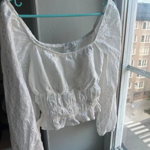 Vit blus från Chiquelle - En vit blus från Chiquelle med broderade detaljer och elastisk midja. Blusen har långa ärmar och volangdetaljer vid nederkanten.