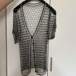 T-shirt aktig coverup med hål runt hela och pärlor - T-shirt aktig coverup med hål runt hela och pärlor. Det är även knappar i mitten av tröjan så du kan ha tröjan öppen eller stängd. Jätte söt coverup som du kan ha med ett linne eller klänning eller vad som passar bäst för dig. 