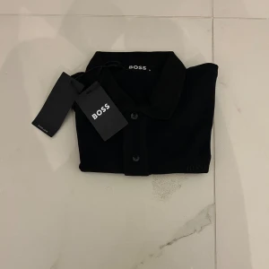 Svart kortärmad skjorta från BOSS - En elegant och stilren svart kortärmad skjorta från BOSS. Skjortan har en klassisk krage och knappar framtill. Perfekt för både formella och informella tillfällen.