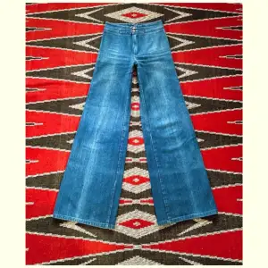 Såå fina ljusblå vida jeans med dubbla knappar från 70-talet. Lite ojämna i färgen (syns på bilderna) men i övrigt är de i dunderskick! 100% bomull broken twill denim. Midja-35cm (+4cm extra sömsmån) Höft-44cm Gren-25cm Längd-107cm Innerben-83cm. 🩵