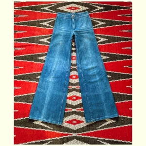 🥚70-tal, Vida Jeans 🥚 - Såå fina ljusblå vida jeans med dubbla knappar från 70-talet. Lite ojämna i färgen (syns på bilderna) men i övrigt är de i dunderskick! 100% bomull broken twill denim. Midja-35cm (+4cm extra sömsmån) Höft-44cm Gren-25cm Längd-107cm Innerben-83cm. 🩵