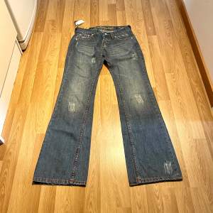 (22) Ljusblåa lågmidjade bootcut jeans med färgade sömmar och små slitningar. Midjemått rakt över: 37 cm, innerbenslängd: 85cm 🩵
