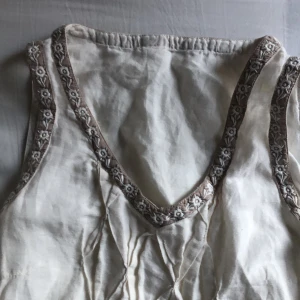 Vit klänning - En klänning som blivit färgad med te vilket gett den en creme liknande färg. Fina detaljer och väldigt skönt linne-material. En liten fläck har den dock på framsidan