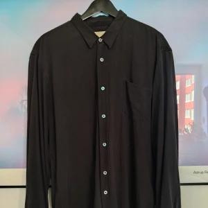 Our Legacy Silk Shirt storlek 52 - Our Legacys klassiska skjorta i svart. Avslappnad passform. 100% kinesiskt råsilke. Knappar i pärlemor. Använd flera gånger, men utan skador eller slitningar.  https://www.ourlegacy.com/classic-shirt-black-silk-core