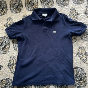 Mörkblå Lacoste piké  - Hej säljer min mörkblåa Lacoste piké eftersom den blivit för liten. Det är en perfekt kortarmad pike nu inför sommaren. Den är jätte bra skick och köpte den för nypris 749kr